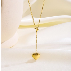 Detalle de collar con colgante de corazón dorado pulido sobre fondo de seda blanca