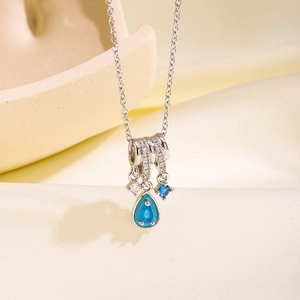 Silberhalskette mit Zirkon-Ringen und blauem Tropfenanhänger auf Seidenstoff