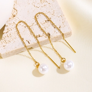 Elegant gold chain drop earrings with white pearls displayed on a textured stone base