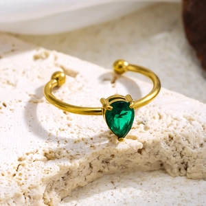 Detailaufnahme von 18K vergoldetem offenem Ring mit Smaragd-Edelstein auf hellem Stein