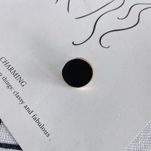Détail de boucles d'oreilles rondes en émail noir avec bordure dorée sur carte d'affichage
