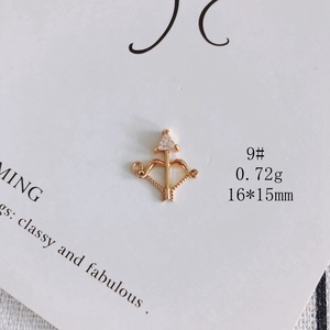 Macro detail of a 16x15mm gold-plated bow and arrow charm with triangular zircon stone