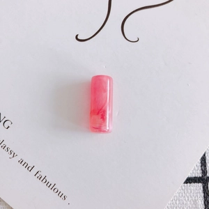 Dettaglio di una perla cilindrica in resina marmorizzata rosa per gioielli fai-da-te
