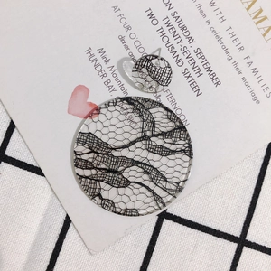 Détail de boucles d'oreilles rondes en résine avec dentelle noire sur fond vintage