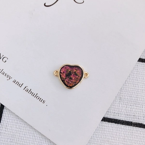 Detail of heart-shaped gold-rimmed charm with pink gold foil sequins for DIY jewelry