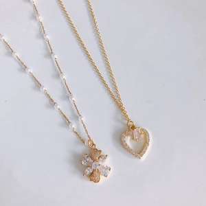 Gold plated floral pendant with rhinestones and heart necklace with crystals on white background