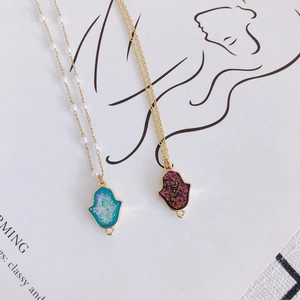 Pendentifs main de Hamsa avec bordures dorées et perles sur fond de magazine minimaliste