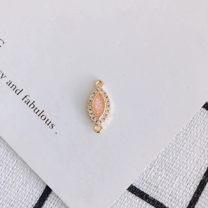 Detailed view of pink resin marquise charm with gold trim and white zircon accents