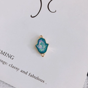 Gros plan d'un pendentif Main de Fatma bleu paon aux bords dorés sur tissu blanc