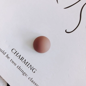 Detail of matte reddish-brown circular resin stud accessory on minimalist display card