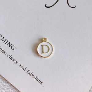 Dettaglio del ciondolo tondo in smalto bianco con lettera D dorata per gioielli fai-da-te