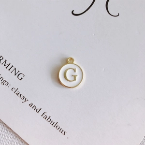 Dettaglio del ciondolo rotondo in smalto bianco con lettera G dorata per gioielli fai da te
