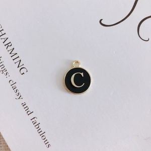 Detail of round gold metal charm with black oil drip and gold letter C for DIY jewelry
