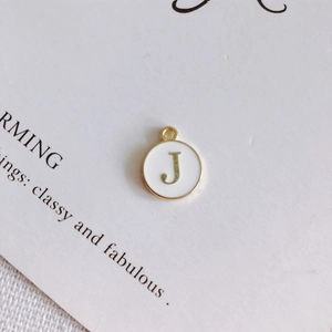Dettaglio del ciondolo rotondo in smalto bianco con lettera J e bordo dorato per gioielli DIY