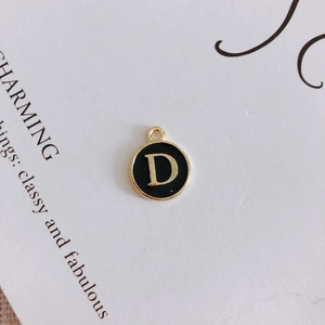 Macro detail of round black enamel letter D charm with gold-plated metal alloy borders