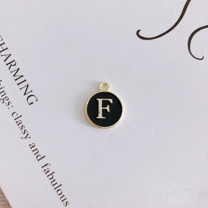 Macro detail of a round black enamel letter F charm with golden metal border