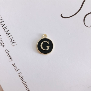 Macro view of a gold-toned alloy charm with black enamel and white letter G detail