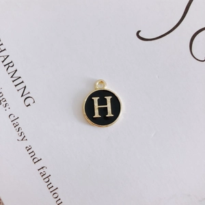 Close-up of a round black enamel pendant featuring a gold letter H on a white card
