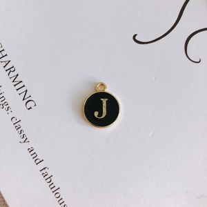 Detailed macro shot of a black enamel round pendant featuring a golden letter J charm