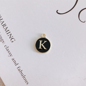 Detail of round black enamel pendant with golden letter K for DIY jewelry projects