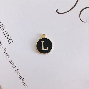 Close-up of a round black enamel letter L charm with a gold metal frame for DIY jewelry