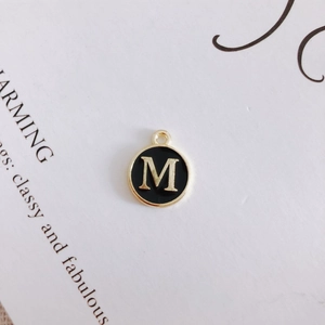 Macro shot of a black enamel round pendant with gold letter M for DIY jewelry making