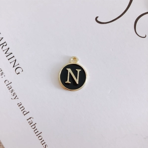 Close-up of a round black enamel letter N pendant with gold-toned alloy edges
