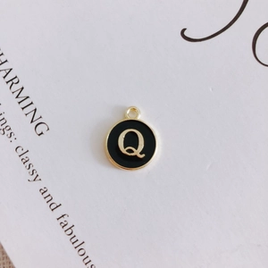 Detail of round black enamel pendant with gold letter Q and metal frame for DIY jewelry