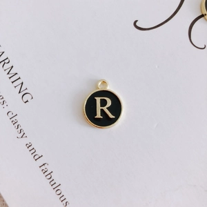 Close-up of golden letter R round charm with black enamel inlay for DIY jewelry