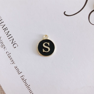 Macro shot of a round black enamel letter S pendant with gold metal edges and hanging loop