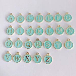 Flat lay of 26 round mint green enamel letter charms with gold alloy frames for DIY jewelry