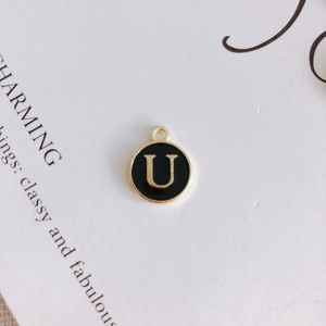 Macro detail of round gold-plated alloy pendant with black enamel and letter U