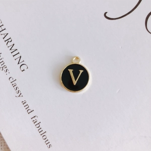 Macro detail of a round black enamel pendant with gold letter V for DIY jewelry making