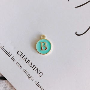 Detail of round golden letter B pendant with light blue enamel on white display card
