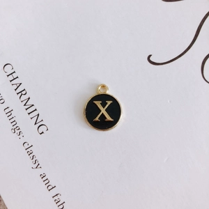 Detail view of round black enamel letter X charm with gold-plated metal alloy finish