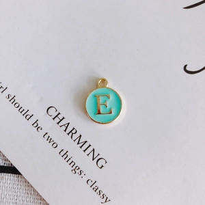 Macro view of mint green enamel letter E round pendant on decorative white card