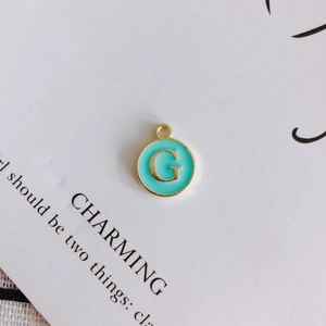 Macro view of mint green enamel G letter pendant with gold trim for DIY jewelry