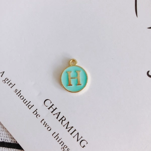 Detailed close-up of a round mint green enamel pendant with golden letter H for DIY jewelry