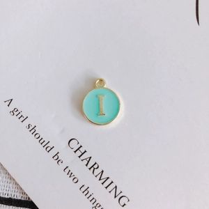 Detailed macro view of mint green enamel round pendant with gold letter I charm
