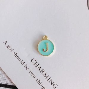 Detailed close-up of a mint green enamel round pendant with a gold letter J charm