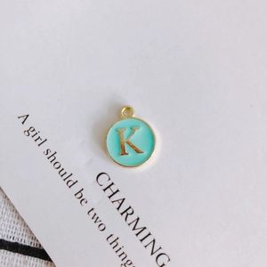 Macro detail of a round green enamel pendant featuring a gold letter K charm component