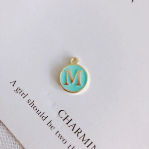 Close-up of a round green enamel pendant with gold letter M for DIY jewelry making