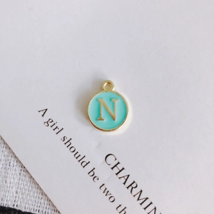 Macro shot of a round gold-rimmed mint green enamel pendant with a golden letter N