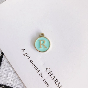 Detail of round mint green enamel letter R charm pendant with gold metal finish