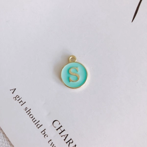 Detailed close-up of a round gold-rimmed light green enamel pendant with letter S engraving