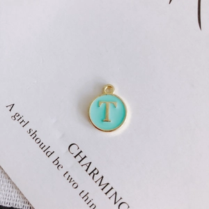 Macro detail of mint green enamel letter T round pendant in gold plated alloy for DIY jewelry