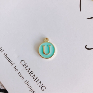 Detail of a round gold-plated alloy pendant with sky blue enamel and letter U inlay