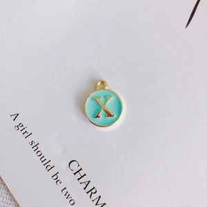 Macro detail of round gold-plated alloy pendant with light blue enamel and letter X