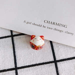 Close-up of a handmade ceramic Maneki-Neko bead with red floral pattern for DIY jewelry