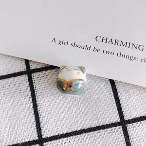 Close-up of a handmade ceramic fortune cat bead with floral patterns and gold details